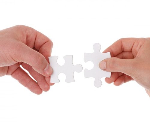 Two hands holding white puzzle pieces